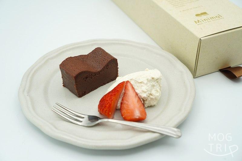 ビーントゥバーチョコレート専門店 Minimal（ミニマル）の生ガトーショコラが生クリームと苺と一緒にさらに載せられ、テーブルに置かれている