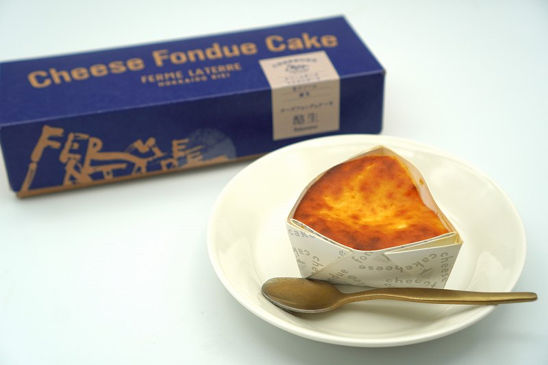 フェルム ラ・テール美瑛のチーズフォンデュケーキ酪生の箱とチーズケーキがテーブルに置かれている