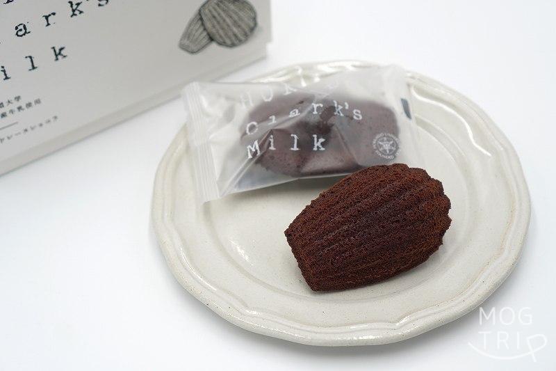 北海道大学の敷地内にある北大マルシェ の「HOKUDAI Clark's Milk マドレーヌ ショコラ」が皿にのせられ、テーブルに置かれている