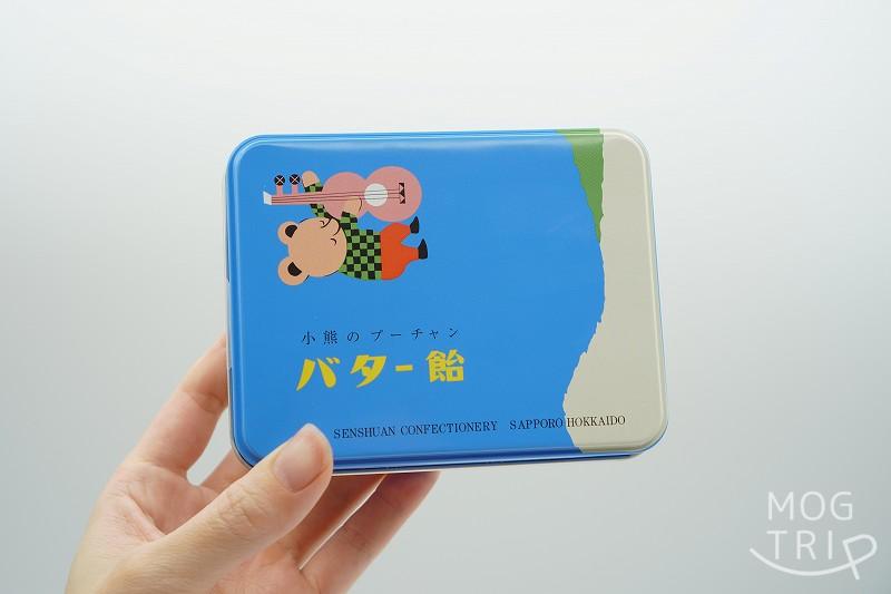 札幌千秋庵の「小熊のプーチャンバター飴」の缶を手に持っている様子