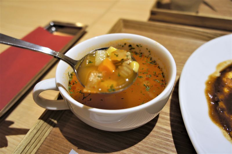 きのとやファーム店の「おいしいたまごの大人のオムライス トマトチキンスープ付」のスープを、スプーンですくっている様子