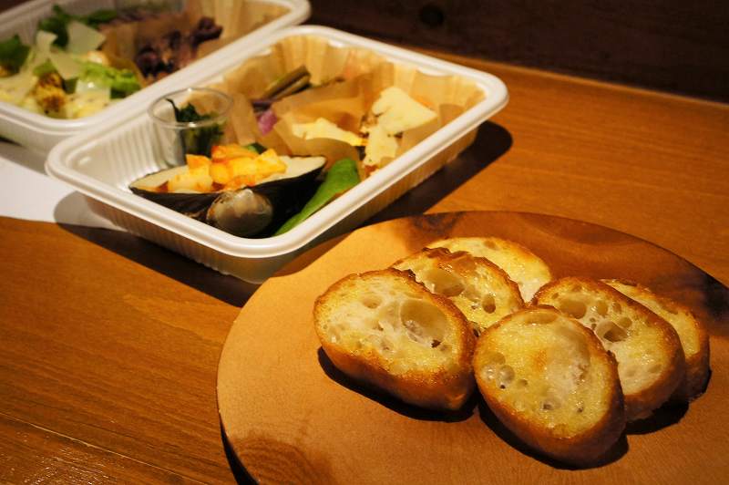 バゲットがのった木の皿と前菜が入ったプラスチックケースがカウンターに置かれている
