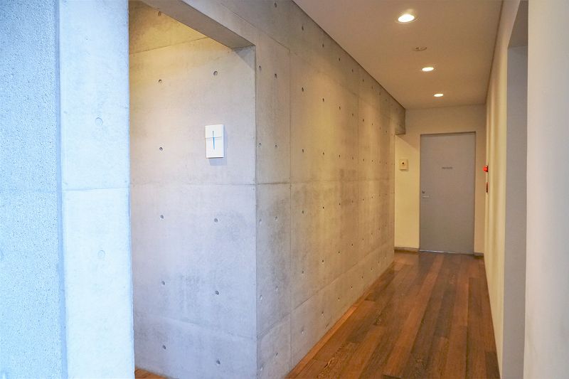 コンクリートの壁と木の床の、六花亭 真駒内六花亭ホール店のトイレ前