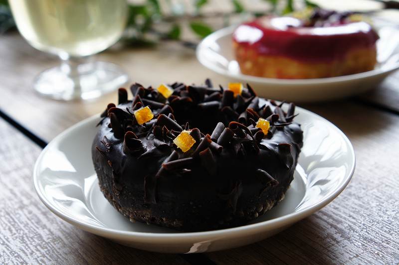 チョコレートやオレンジがトッピングされた黒色のドーナツがテーブルに置かれている