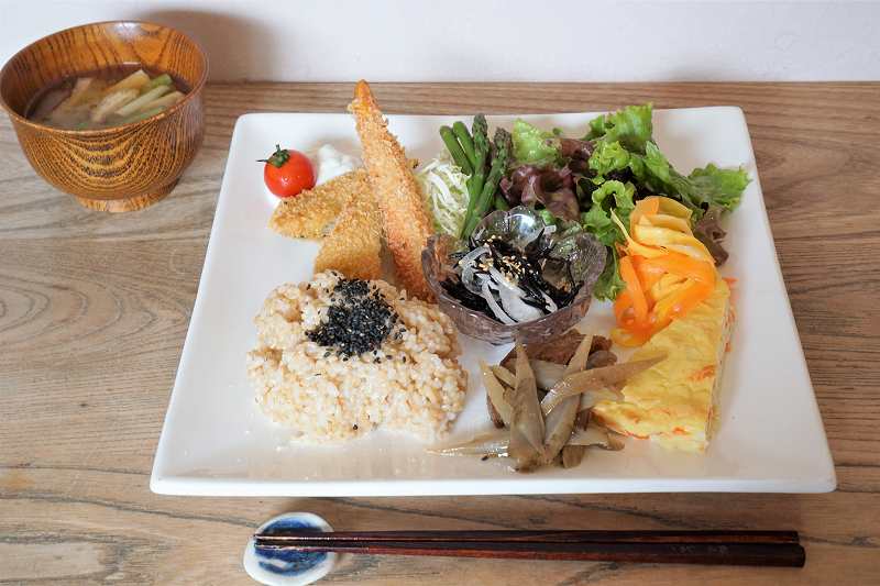 玄米ごはんや野菜のおかずのプレートと味噌汁がテーブルに置かれている