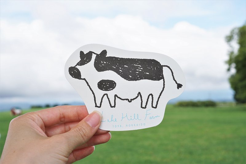 牛のイラストが描かれたレークヒルファームのショップカードを手に持っている様子