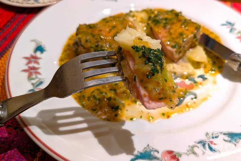 フランス料理店mondo（モンド）のメイン料理「恵庭産 “米豚三源とん” のロースト シャルキュティエール風」を、フォークで持ち上げている様子