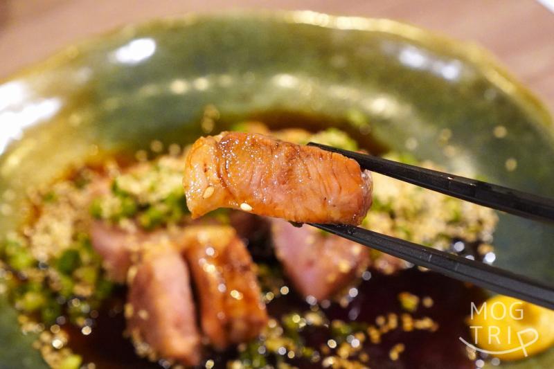 和菜酒房おりべの、旭川産 いも豚 肩ロースたれ焼きを箸で持ち上げている様子