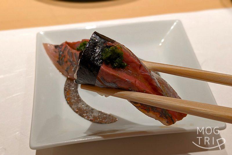 札幌すすきのにある「まる鮨」のアジの握りを箸で持ち上げている様子