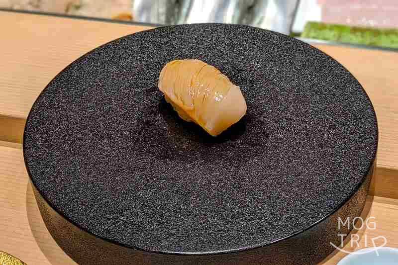 札幌すすきのにある「まる鮨」のホタテの握りがテーブルに置かれている