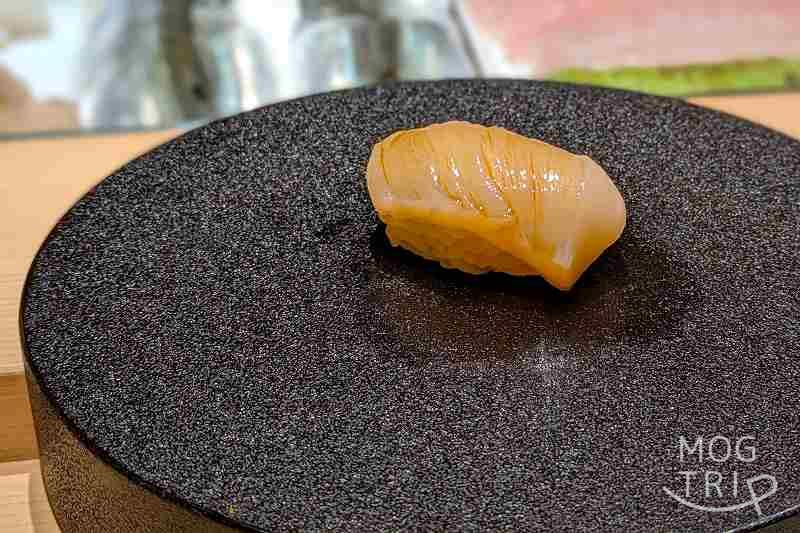 札幌すすきのにある「まる鮨」のホタテの握りがテーブルに置かれている